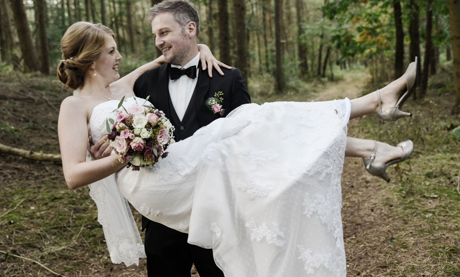 Hochzeitsfoto Brautpaar Shooting Ehemann trägt Braut auf Händen im Wald