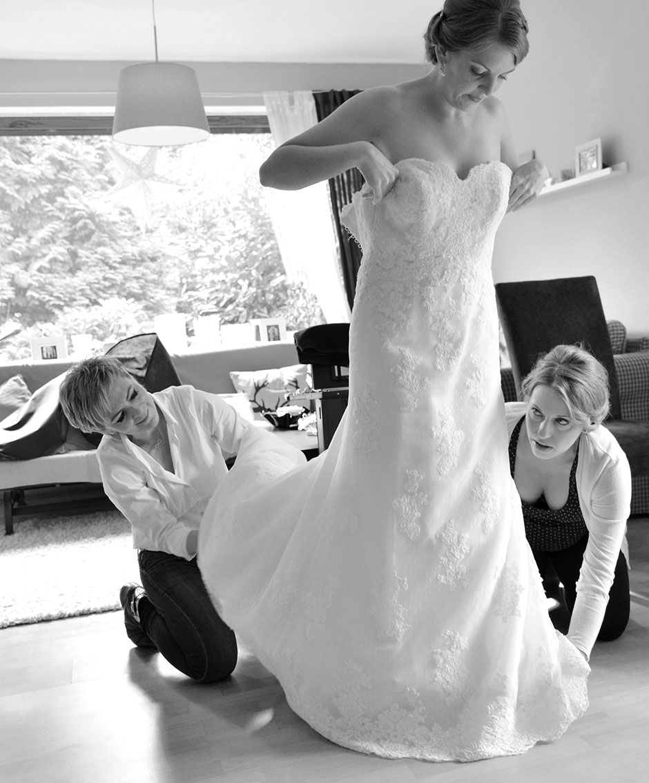 Hochzeitsfoto Brautstyling Braut zieht Hochzeitskleid an zuhause